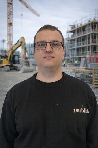 Mann med briller og svart genser, på en byggeplass