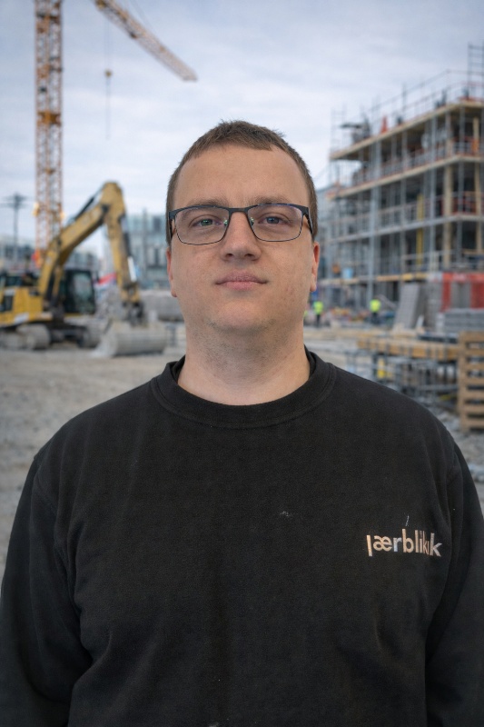 Mann med briller og svart genser, på en byggeplass
