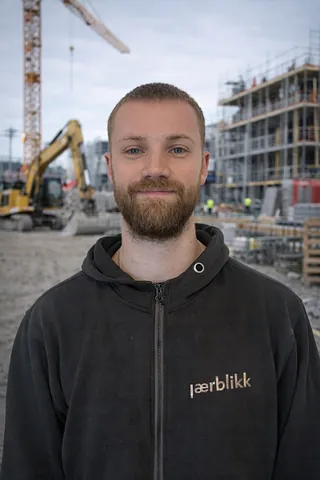 Mann med brunt hår og svart genser, på en byggeplass
