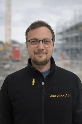 Mann med briller, brunt hår og svart genser, på en byggeplass